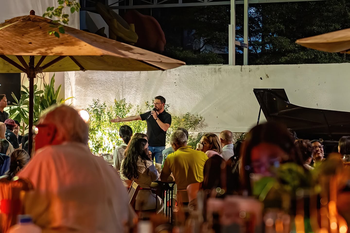 Live concert night at Bellini — host speaking to a packed garden crowd with grand piano